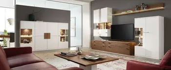Wohnzimmer mit weißer Wohnwand, TV-Möbel in Holzoptik, beleuchteten Vitrinen und Couchtisch zwischen roten Sesseln.